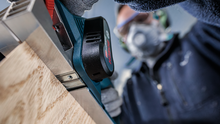 佩戴安全设备的人员使用电动刨床刨削木板。