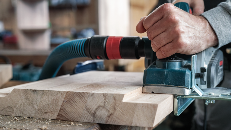 一名工人在车间使用电刨刨平木板。