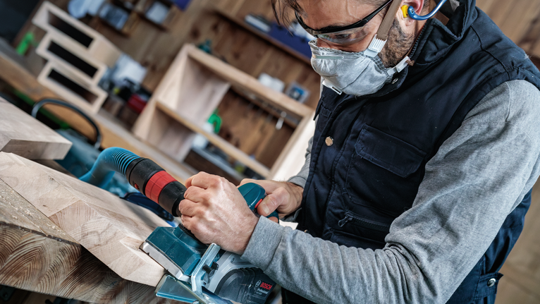 佩戴安全设备的人员操作电锯切割木板。