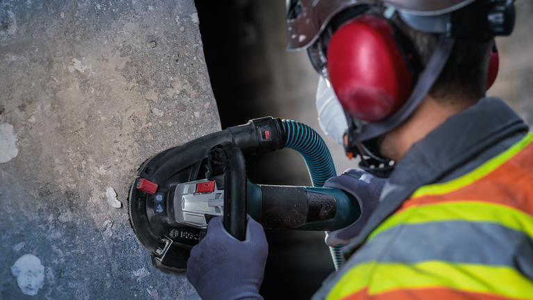 工人佩戴安全设备，用手持式电动研磨机打磨混凝土。.