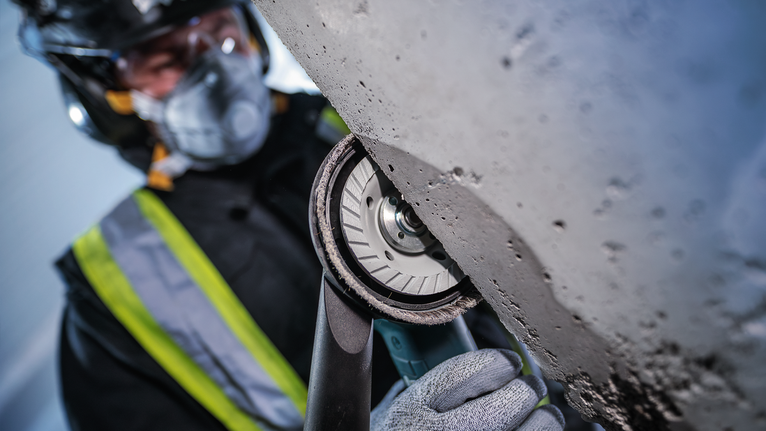 佩戴安全设备的人员使用手持电动工具打磨混凝土。.