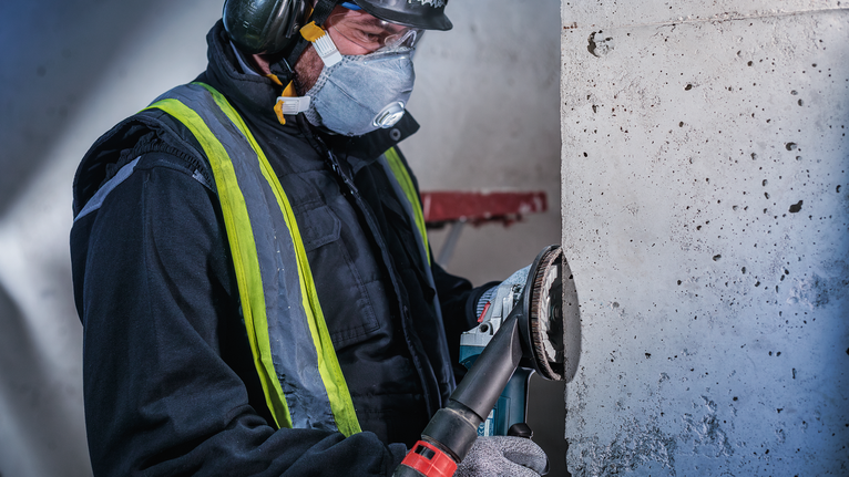 工人佩戴安全设备，用电动工具打磨混凝土墙。.