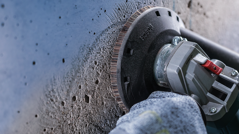 佩戴安全设备的人员使用角磨机打磨混凝土墙。.