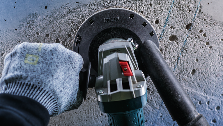 一名佩戴安全设备的工人正在用电动工具打磨混凝土墙。.