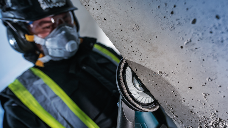 佩戴安全设备的人员使用电动工具打磨混凝土表面。.