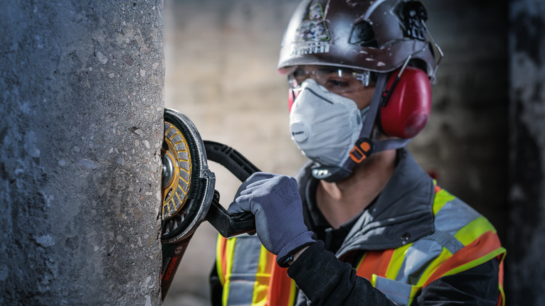 一名佩戴安全设备的人员正在使用电动工具打磨混凝土柱。