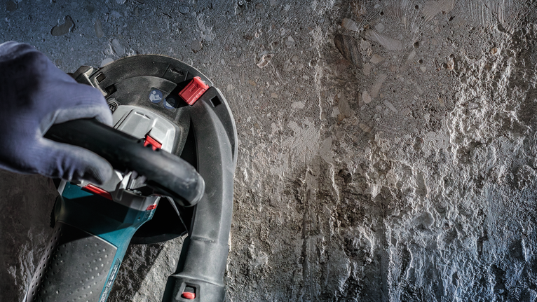 佩戴安全设备的人员在粗糙的混凝土墙上操作电动工具。