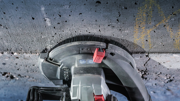 电动工具沿混凝土表面打磨，可见除尘刷附件。