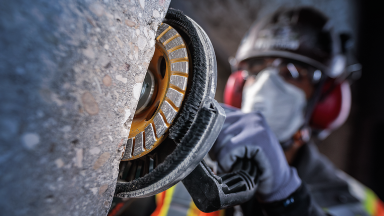 一名佩戴安全设备的人员正在使用电动工具打磨混凝土墙。