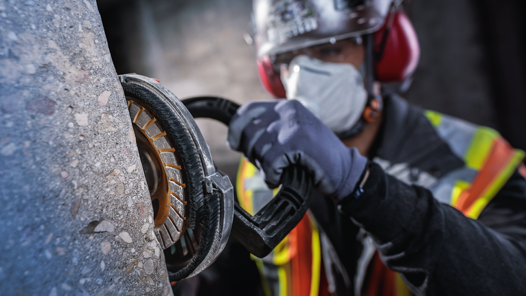 佩戴安全设备的人员使用电动工具研磨混凝土。