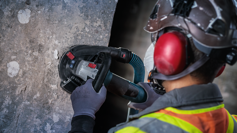 佩戴安全设备的人员使用电动工具打磨混凝土墙。