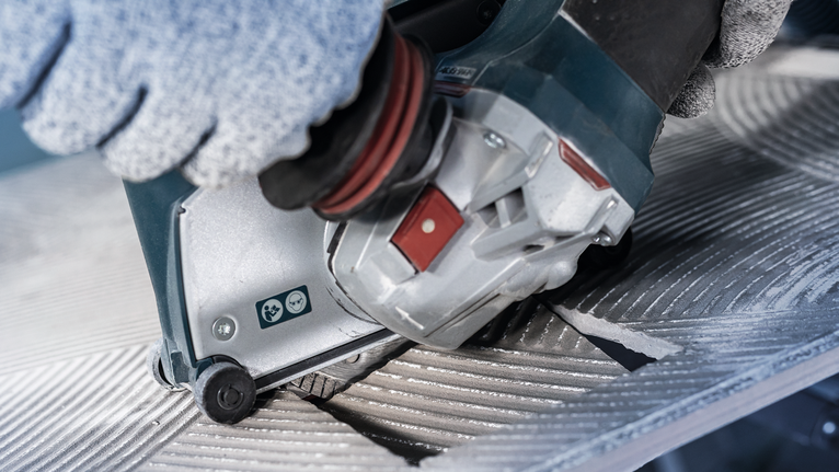 佩戴安全设备的人员操作电动工具切割有凹槽的金属表面。