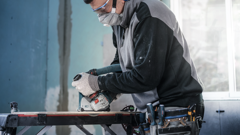 佩戴安全设备的人员使用圆锯在工作台上切割木材。