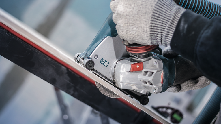 佩戴安全设备的人员使用电动工具切割金属棒。