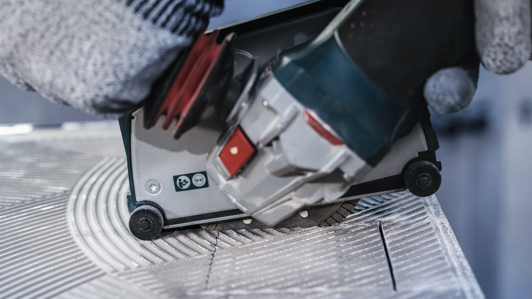 佩戴安全设备的人员引导电动工具在瓷砖上切割凹槽。