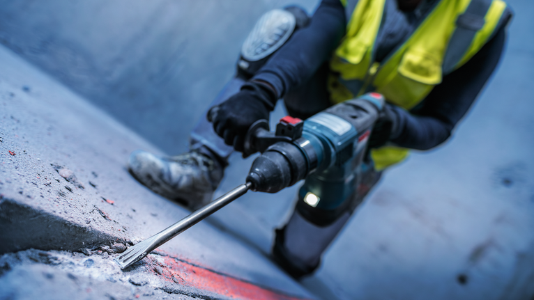 一名佩戴安全设备的人员用旋转锤凿击混凝土表面。