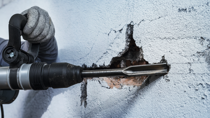 一名佩戴安全设备的人使用旋转锤凿墙。