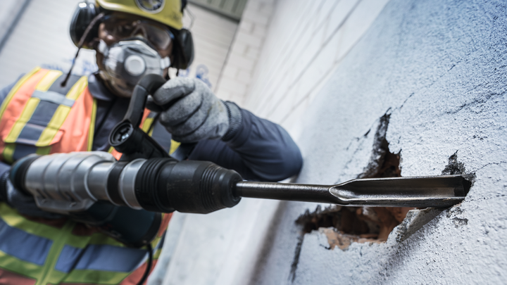 佩戴安全设备的人员使用旋转锤打破混凝土墙。