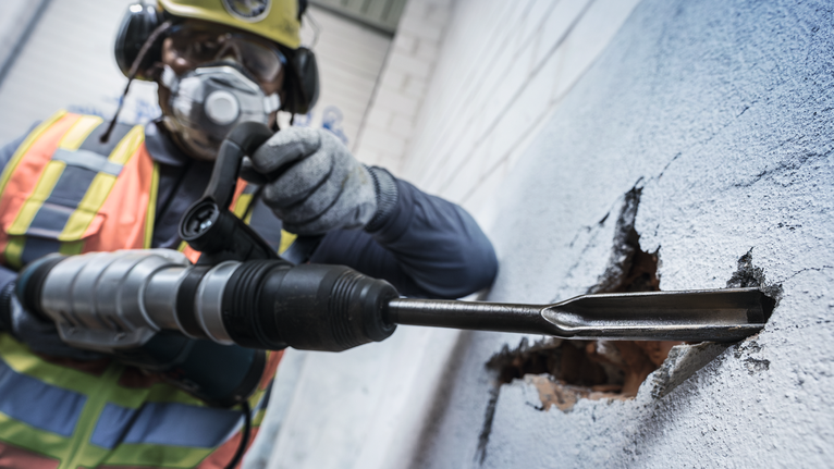 佩戴安全设备的人员使用旋转锤打破混凝土墙。