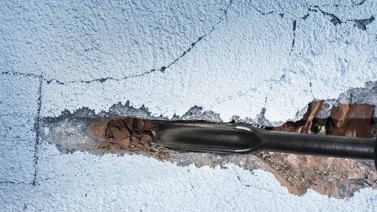 凿子工具打破了粉刷过的墙壁上的灰泥。