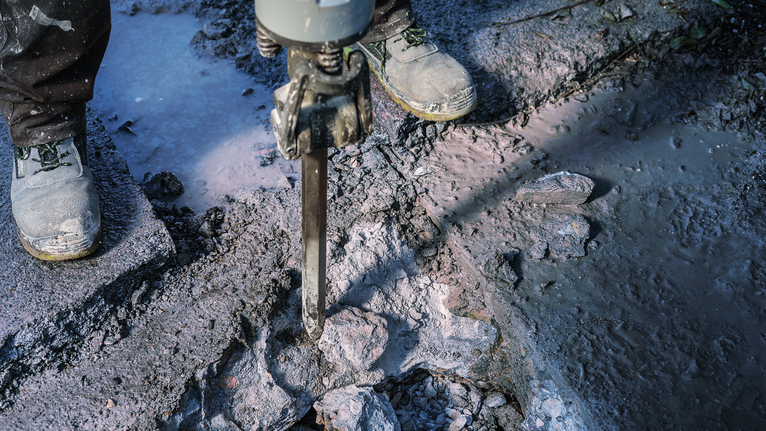 佩戴安全设备的人员用破碎锤破碎混凝土。