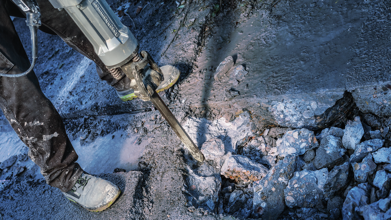 佩戴安全设备的人员使用破碎锤破碎混凝土。.