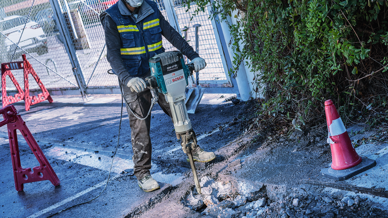 一名佩戴安全设备的人员使用动力拆除工具破碎混凝土。
