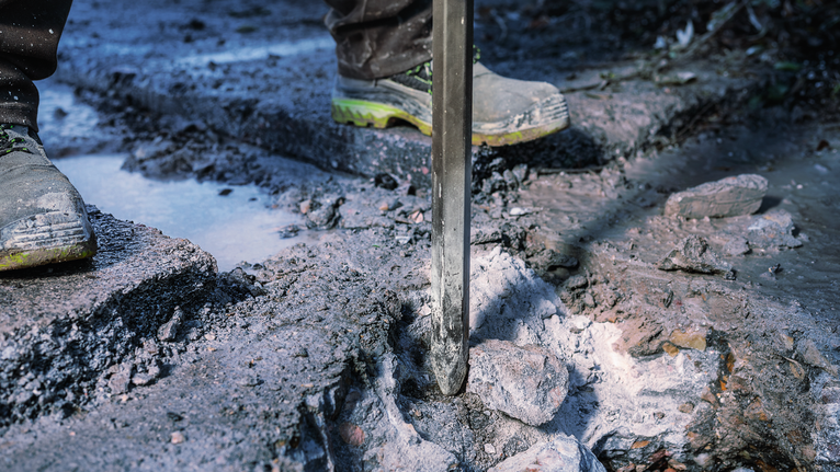 一名佩戴安全设备的人员在户外使用拆除工具破碎混凝土。