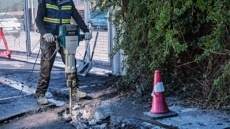 一名佩戴安全设备的人员正在用破碎锤破碎混凝土。