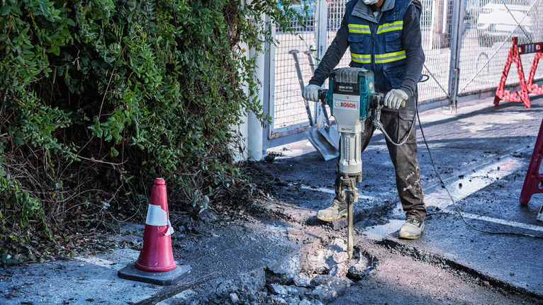 一名佩戴安全设备的人员使用拆除工具破碎混凝土。