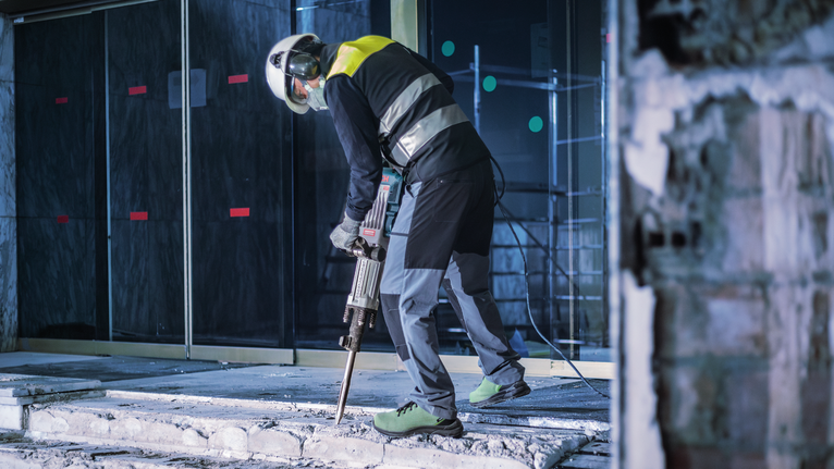 佩戴安全设备的人员用破碎锤破碎混凝土。.