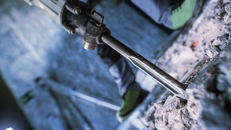 佩戴安全设备的人员使用破碎锤破碎混凝土。