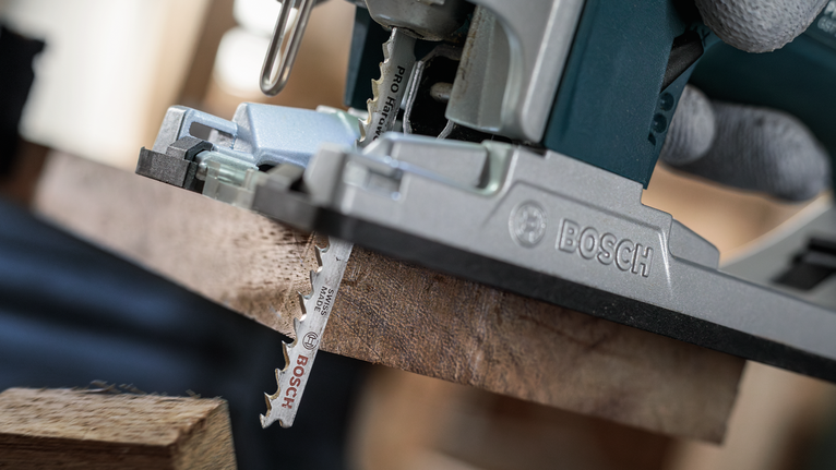 佩戴安全设备的人员使用曲线锯切割木板。