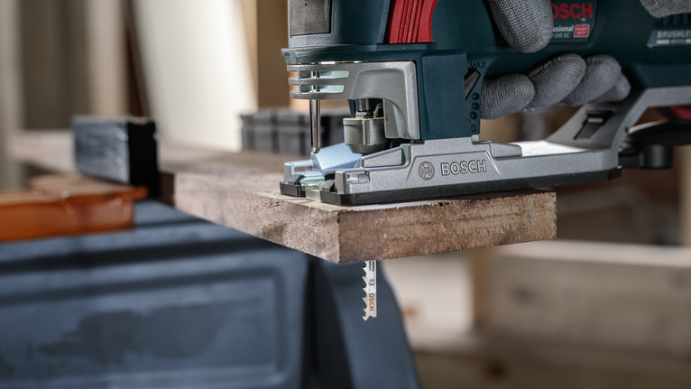 佩戴安全设备的人员使用曲线锯切割木板。