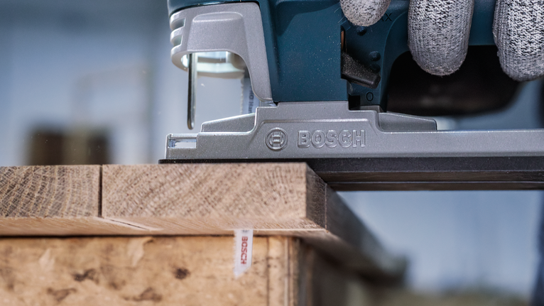 佩戴安全设备的人员使用曲线锯切割木板。