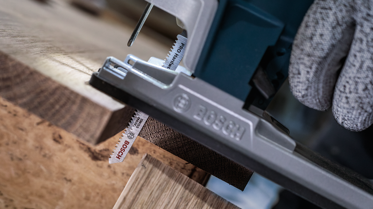 佩戴安全设备的人员使用曲线锯切割木板。