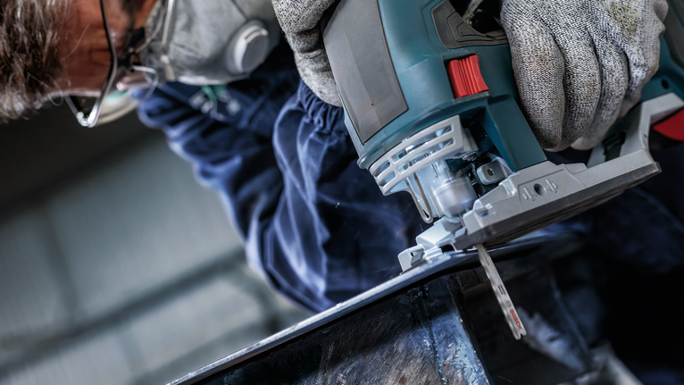 佩戴安全设备的人使用曲线锯切割金属。