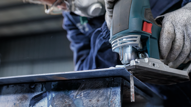 佩戴安全设备的人使用曲线锯切割金属板。