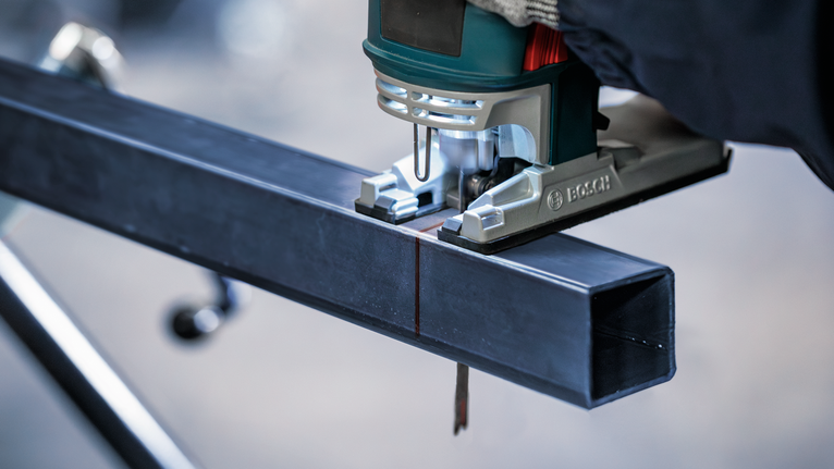 佩戴安全设备的人员使用曲线锯切割金属梁。