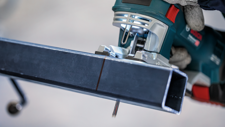 佩戴安全设备的人员使用曲线锯切割金属梁。