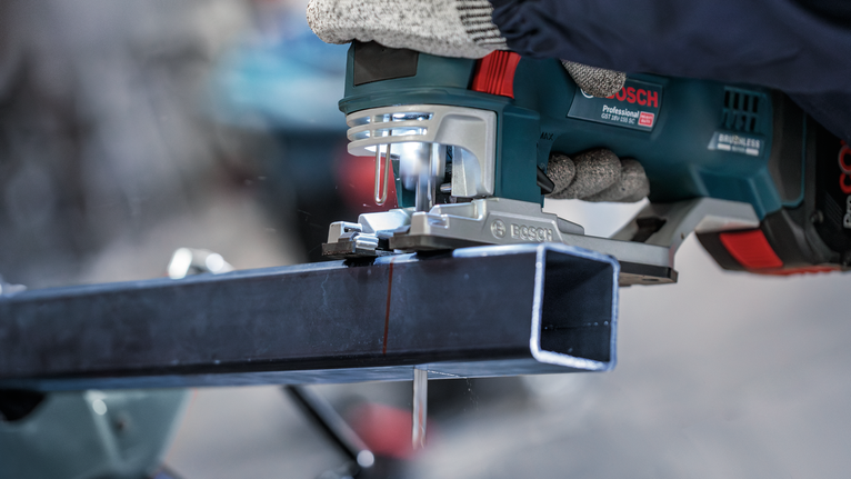 佩戴安全设备的人员使用手持电锯切割金属梁。