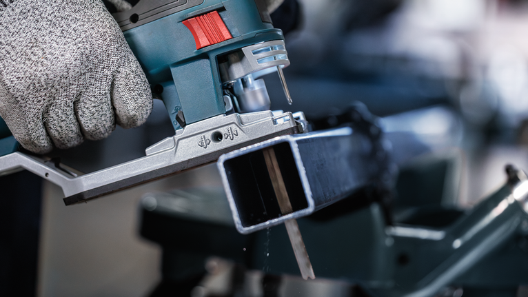 佩戴安全设备的人员使用曲线锯切割金属梁。