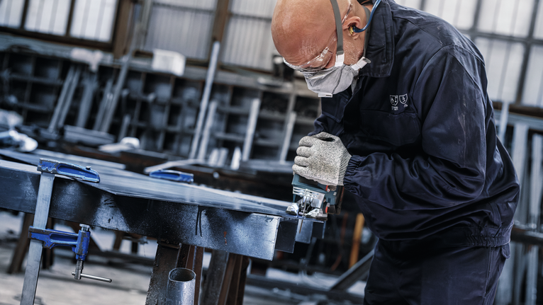 佩戴安全设备的人员在车间使用电锯切割金属。