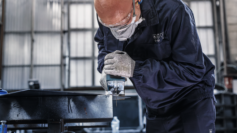 佩戴安全设备的人员使用手持电锯切割金属。