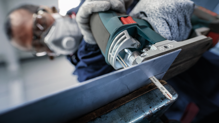 一名佩戴安全设备的人使用曲线锯切割一块金属板。