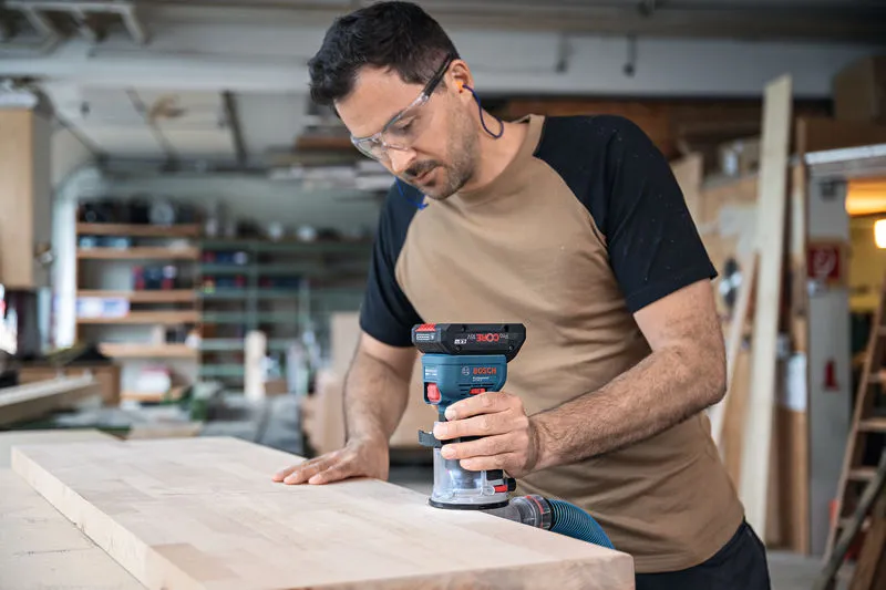 一名佩戴安全设备的人员使用无绳掌上路由器对木板的边缘进行布线。.