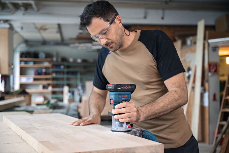 一名佩戴安全设备的人员使用无绳掌上路由器对木板的边缘进行布线。.