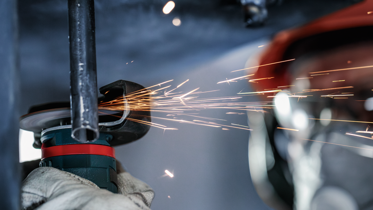 工人佩戴安全设备研磨金属管，产生火花。.