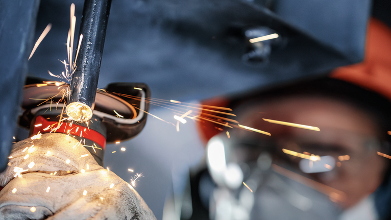 佩戴安全设备的人员研磨金属管，产生明亮的火花。