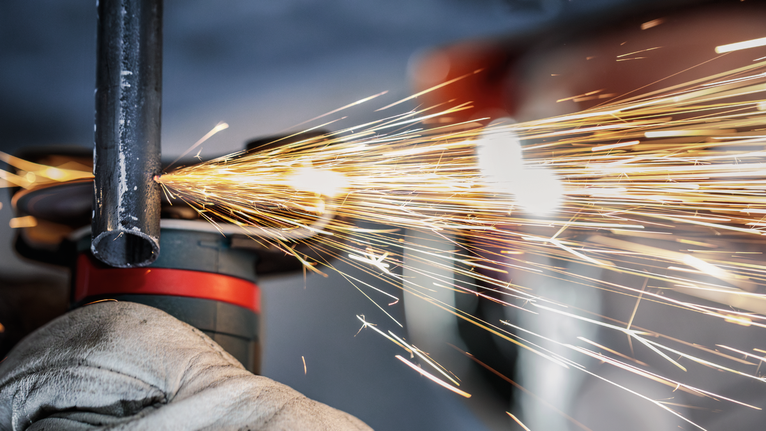 佩戴安全设备的人员研磨金属管，产生明亮的火花。